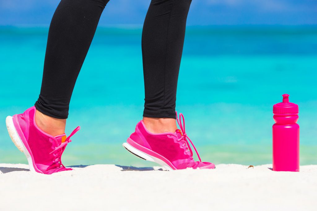 Close-up of female legs in sneakers running on white sandy beach