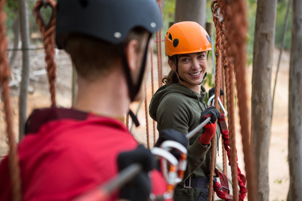 Smiling young woman looking at man while crossing zip line