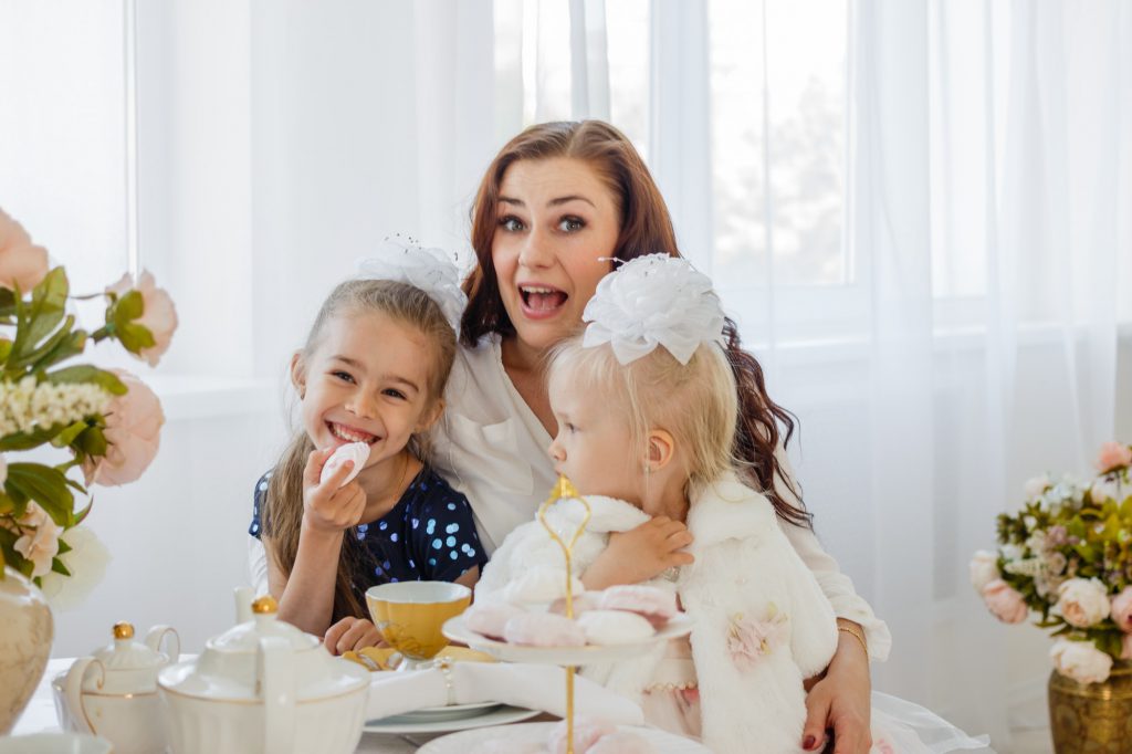 Family portrait of mother and two little daughters at the tea table